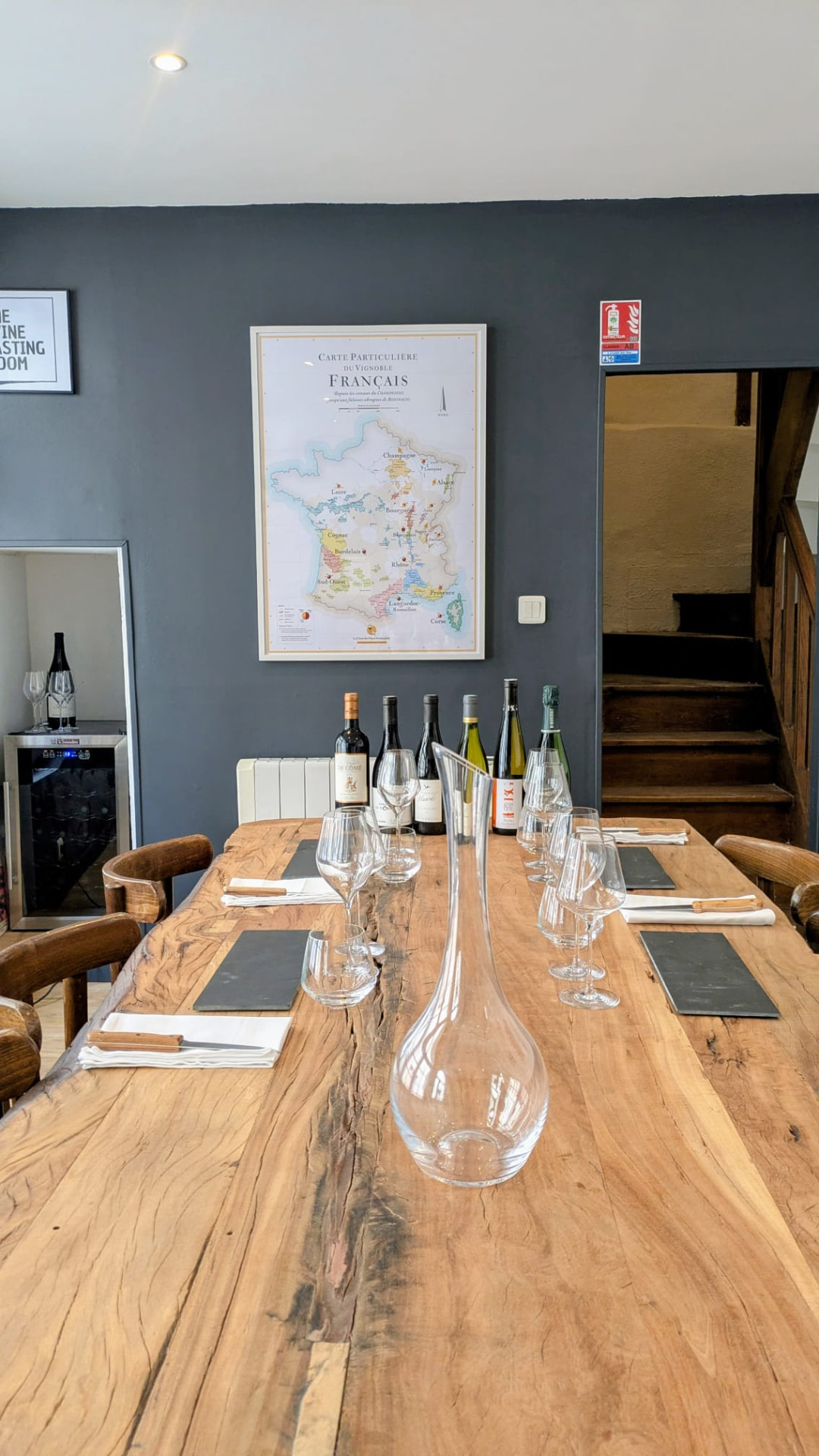 La grande table de The Wine Tasting Room à Bayeux, avec la carte des vignobles français au mur